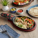 A Choice oval cast iron fajita skillet with chicken, vegetables, and tortillas on a table.