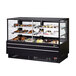 A black Turbo Air bakery display case with refrigerated and dry sections filled with different types of cakes.