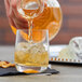 A hand pouring whiskey into a Stolzle Weinland rocks glass filled with ice