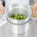 A person using a Vollrath pasta cooker to steam broccoli.
