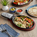A Choice pre-seasoned cast iron fajita skillet with chicken, vegetables, and tortillas on a table.