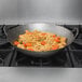 A Town hand hammered wok filled with noodles and carrots on a gas stove.