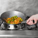 A hand using a Town Carbon Steel Mandarin Wok to cook shrimp and vegetables.