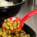 A red Thunder Group perforated salad bar spoon with green olives in it over a bowl of green olives.