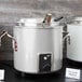 A large silver Vollrath stock pot with a metal handle and lid.