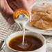 A person pouring International Delight Caramel Macchiato creamer into a cup of coffee.