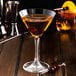 A martini glass with Fabbri Amarena cherries on a wooden surface.