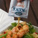 A hand pours Ken's Honey Dijon Mustard Dressing from a packet onto a shrimp salad.