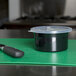 A Carlisle black plastic crock with a lid and a knife on a green cutting board.