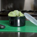 A Carlisle black plastic crock with broccoli inside on a cutting board.