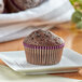 A brown Bake'n Joy double chocolate muffin on a plate with purple wrappers.