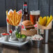 A silver stainless steel round sauce cup with red sauce on a table with a burger and fries.