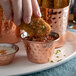 A hand dipping fried chicken into a copper sauce cup.