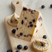 A 2.5 lb. half wheel of Long Clawson White Stilton cheese with blueberries on a wooden board with crackers.