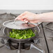 A hand using a Vollrath Optio stainless steel fry pan to cook food on a stove.