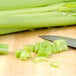 Fresh celery cut into pieces on a cutting board next to a knife.