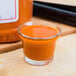 A glass of orange liquid next to a bottle of Sweet Baby Ray's Buffalo Wing Sauce on a counter.