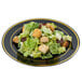 A Fineline Silver Splendor black plastic plate with gold bands holding a salad with lettuce and croutons.