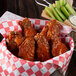 A basket of chicken wings and celery sticks with a bowl of Louisiana Supreme Hot Sauce.