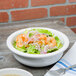 A close up of a Fiesta White China serving bowl filled with salad and shrimp.