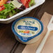 A container of Ken's Foods Bleu Cheese next to a salad.