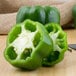 A large green bell pepper cut in half on a white background next to a knife.