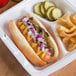 A hot dog with mustard, onions, and B&G San Del sweet peppers in a styrofoam container.