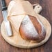 A Rich's white bread loaf wrapped in paper on a wooden cutting board with a knife.