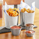 A table with three Acopa stainless steel cups filled with fries and dipping sauce.