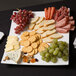 An American Metalcraft square concave melamine platter with cheese, crackers, and grapes.