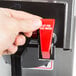 A hand pressing a red button on a Bloomfield automatic coffee brewer.