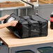 A black soft-sided insulated pizza delivery bag made of heavy-duty nylon, designed to hold up to three 12-inch or 14-inch pizza boxes.