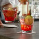 A bartender holding two Anchor Hocking New Orleans Rocks Glasses filled with red liquid and lime slices on a counter.