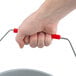 A hand holding a gray Rubbermaid BRUTE bucket with a red handle.