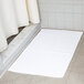 A white Oxford Belleeza bath mat on a tile floor.