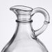 A clear glass Tablecraft olive oil jug with a handle.
