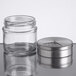 A Tablecraft glass spice jar with adjustable metal lid on a counter.