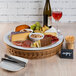 A Frilich tan wicker cooling plate with cheese, crackers, and wine on a table.
