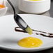 A Mercer Culinary black solid bowl plating spoon with a yellow liquid in the bowl.