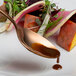 A Mercer Culinary rose gold plating spoon with brown sauce on it being used to plate a vegetable salad.