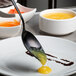 A close-up of a Mercer Culinary black plating spoon over a plate with food on it.