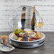 A Frilich clear polycarbonate hinged dome cover over a plate of food and a glass of white wine on a wood table.