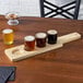 A wooden paddle with four Acopa Beer Tasting Glasses of beer on it.