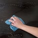 A hand using a blue microfiber cloth to clean a wooden surface.