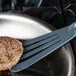 A Mercer Culinary gray slotted turner lifting a hamburger patty from a pan.