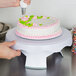 A person using a Wilton plastic cake turntable to decorate a cake.
