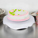 A cake with pink and green frosting on a Wilton plastic cake stand.
