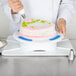 A person using an Ateco plastic cake stand to decorate a cake.
