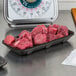 A black CKF foam meat tray on a counter with raw meat.