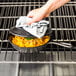 A hand holding a Lodge cast iron skillet with food on a stove.
